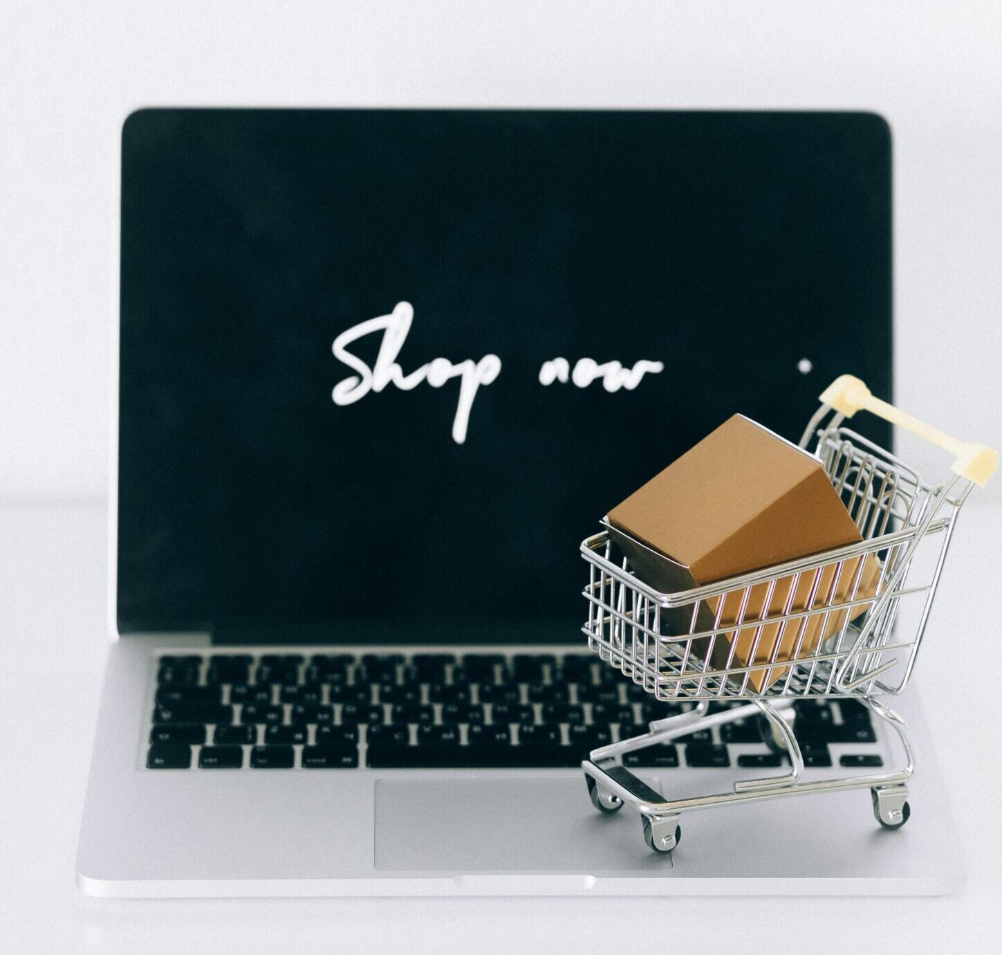 A laptop screen displaying 'Shop now' with a miniature shopping cart and cardboard box.